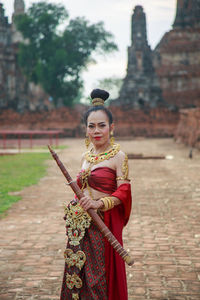 An asian woman in a red thai traditional dress holding an old sword at an ancient ruin temple