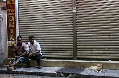 Men sitting on bench against closed shutter