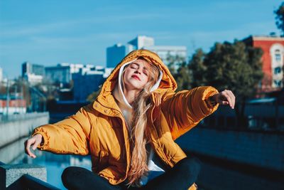 Woman sitting on railing by canal during winter