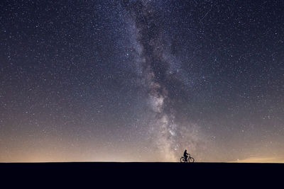 Silhouette man riding bicycle against star field at night