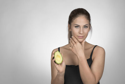 Portrait of young woman holding apple against white background