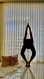 Full length of woman standing against window at home