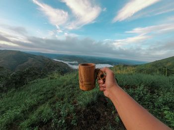 Midsection of person holding umbrella on mountain against sky