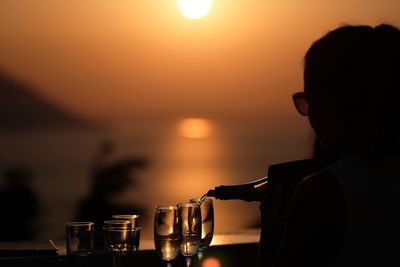 Silhouette man drinking glass against sea during sunset