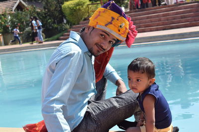 Portrait of man in turban with daughter sitting against swimming pool