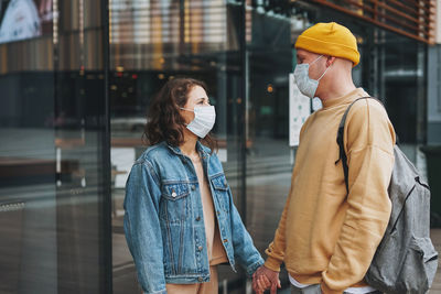 Stylish young family couple hipsters in face mask against glass building, new normal