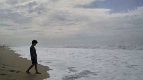 Full length of boy walking on sea shore at beach against sky