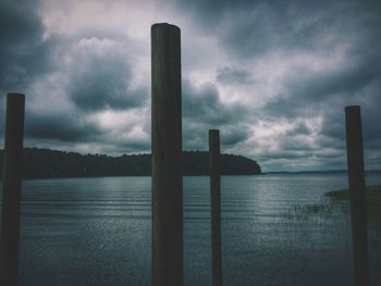 Wooden posts in sea against cloudy sky