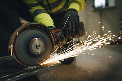 Female worker using electric saw while cutting metal at construction site