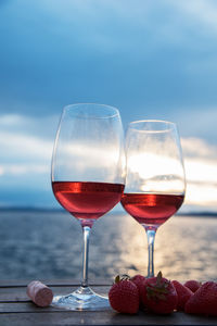 Close-up of red wineglasses by strawberry fruits and cork on table against sky