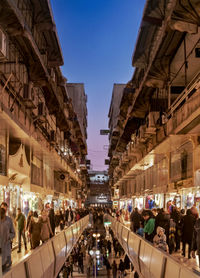 People on street amidst buildings in city at dusk
