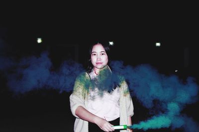 Portrait of young woman holding distress flare at night