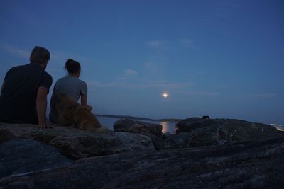 Rear view of young couple sitting dog on rock formation at beach