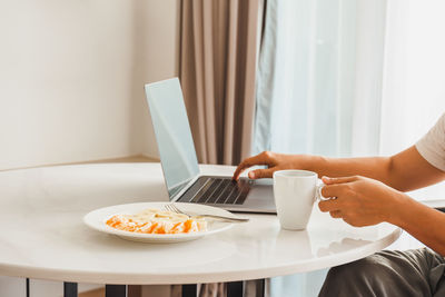 Man having cup of coffee with fresh fruits while working on laptop