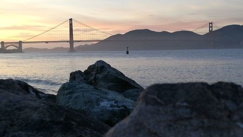 Suspension bridge over sea against sky during sunset