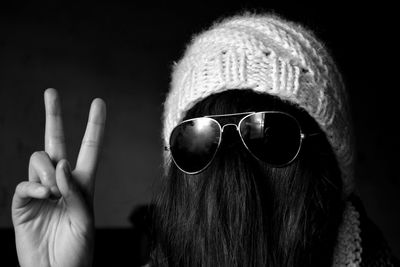Woman with hair on face wearing sunglasses and knit hat while showing peace sign