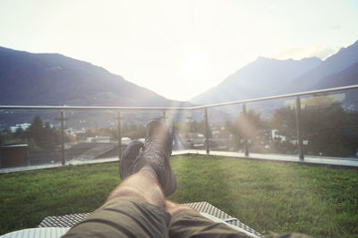 Low section of man relaxing on mountain against sky