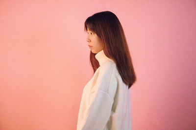 Side view of young woman standing against pink background