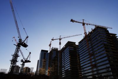 Low angle view of crane by building against clear sky