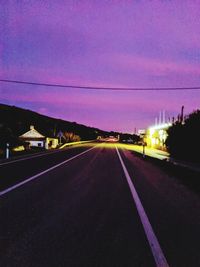 Road by illuminated city against sky at dusk