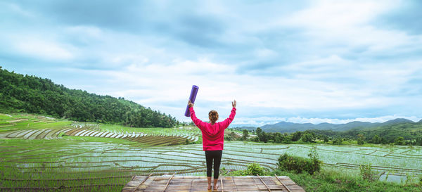 Rear view of woman with arms outstretched standing on field against sky