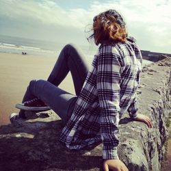 Woman sitting on retaining wall at beach against sky