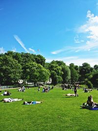 People relaxing at park against sky during sunny day