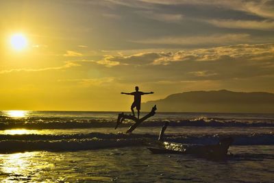 Silhouette man in sea against sky during sunset