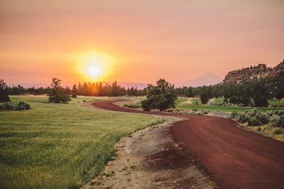 Road amidst field against sky during sunset