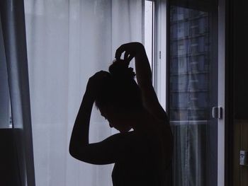 Silhouette woman standing by window at home