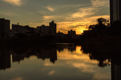 Silhouette buildings by river against sky during sunset