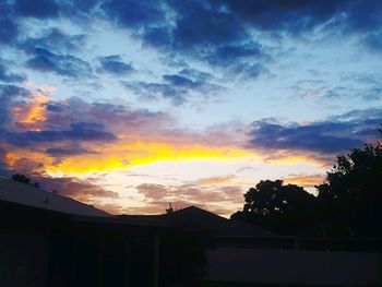 Low angle view of silhouette trees and buildings against sky at sunset