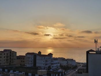 Buildings by sea against sky during sunset