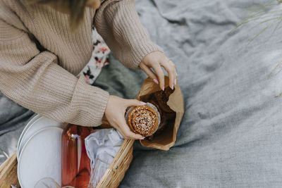 Mid section of woman sitting on blanket and taking cinnamon bun out of paper bag