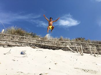 Low angle view of shirtless man jumping over fence at beach against sky