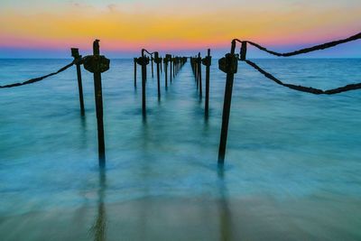 Wooden posts in sea against sky during sunset