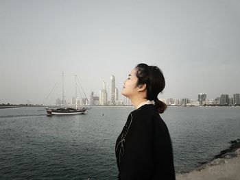 Side view of young woman standing by sea against clear sky