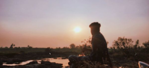 Silhouette man standing on field against sky during sunset