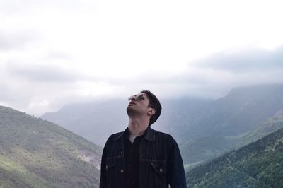 Man in sunglasses standing against mountains during foggy weather
