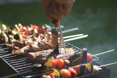 Person holding meat on barbecue grill