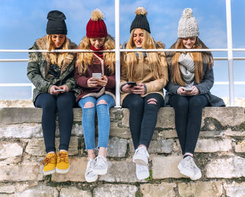 Four friends sitting side by side on a wall text messaging