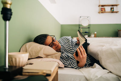 Rear view of man using mobile phone on bed at home