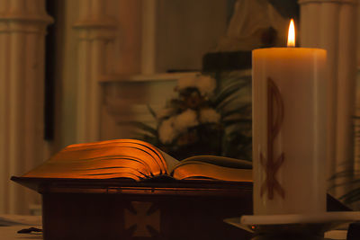 Close-up of lit candle and bible on altar