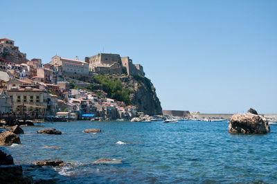 Scenic view of sea by buildings against clear blue sky
