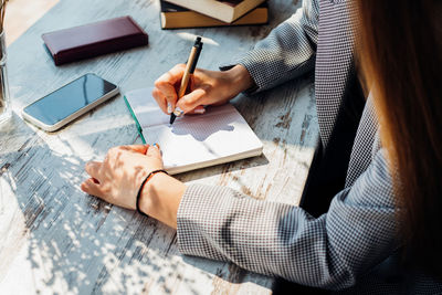 A young woman is sitting at a table writing in a notebook. a business woman works as a freelancer .