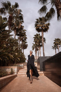 Full length of woman walking on footpath against palm trees