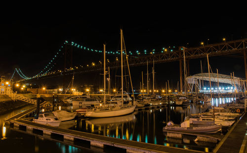 Boats moored on illuminated bridge over river against sky at night
