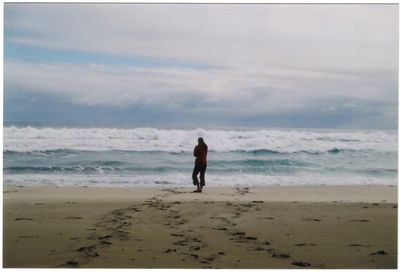 Rear view of man walking on beach against sky