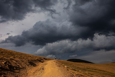 Distant anonymous adventurer walking on sandy path through desert hilly terrain under gloomy dramatic cloudy sky in pyrenees mountains