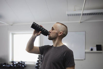 Side view of man drinking water in gym